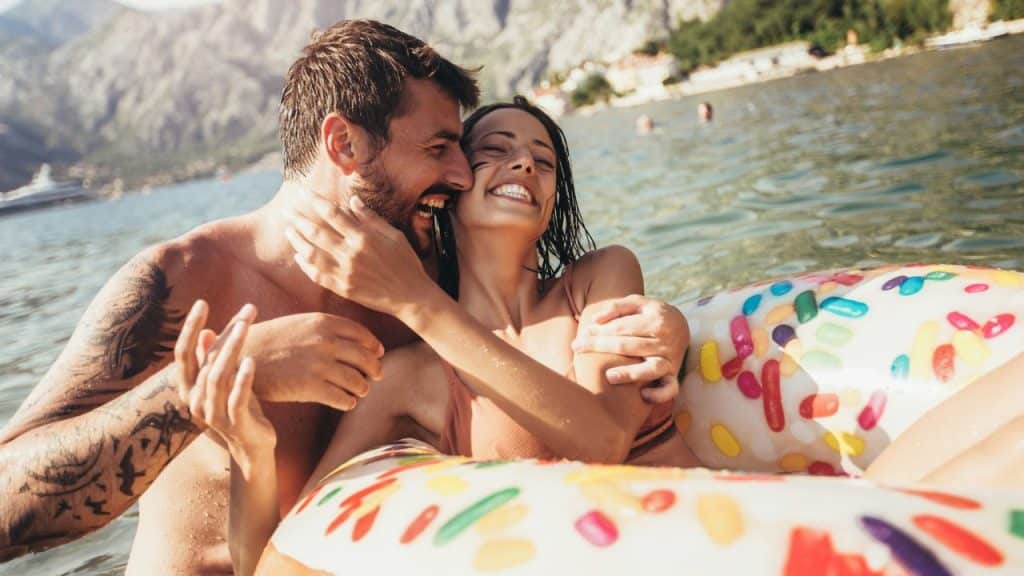 A laughing man and woman embrace while floating on a colorful inflatable ring in the water.