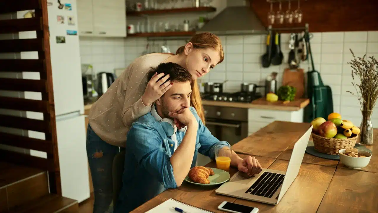 A woman comforting a man as he works on a laptop