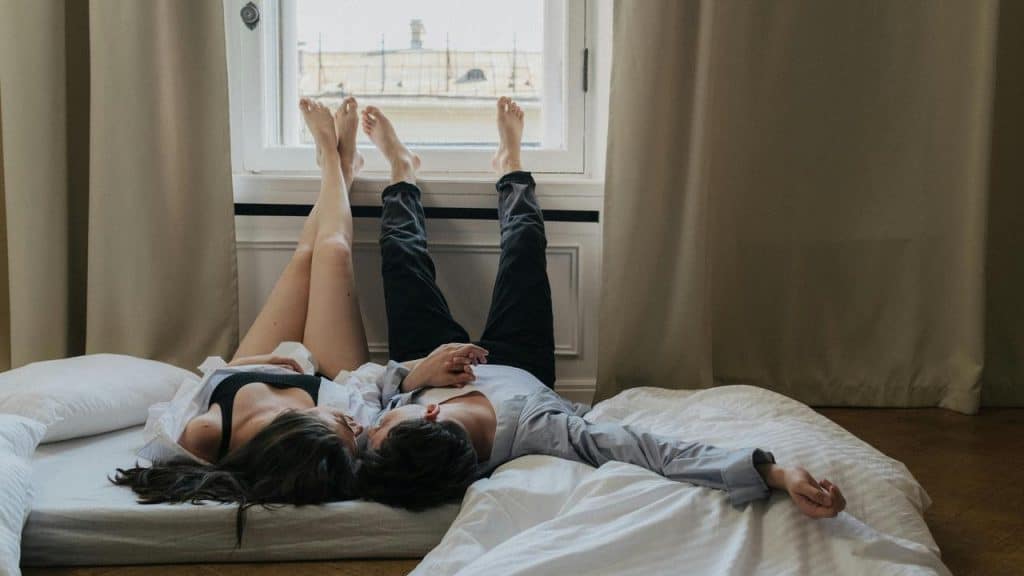 A couple lying on a bed with their legs raised toward a window.