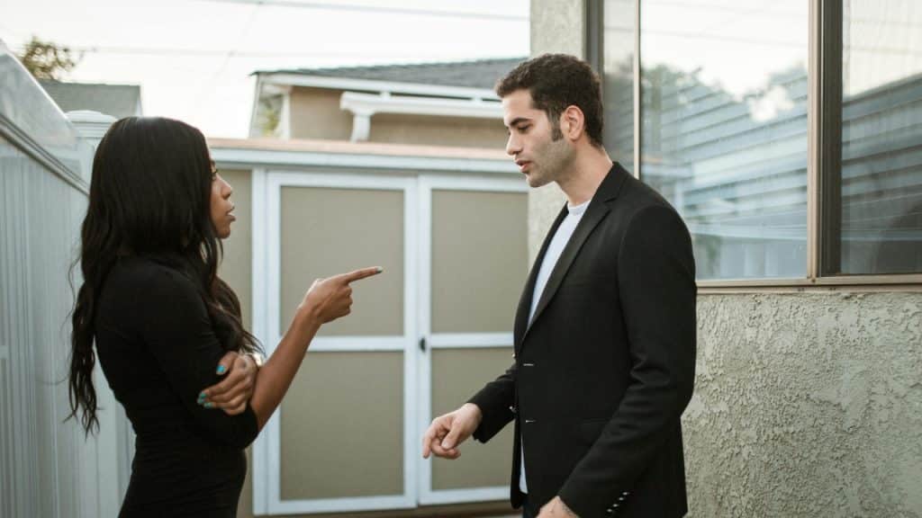 A woman points her finger while talking to a man in a black blazer.