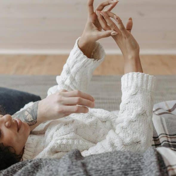 A couple lying under a blanket, with one person looking at their hand.