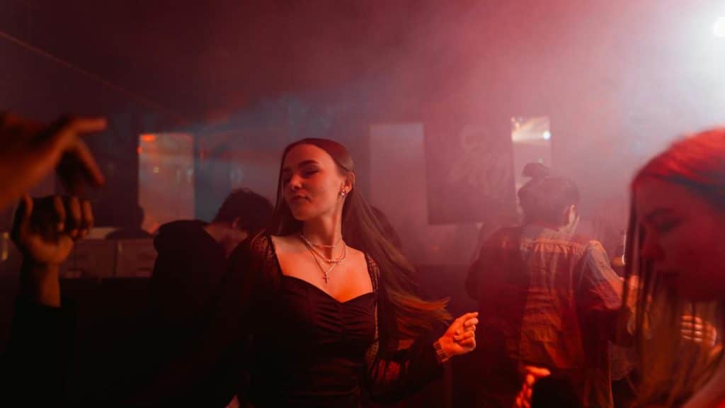A woman dancing in a nightclub with colorful lights and smoke.