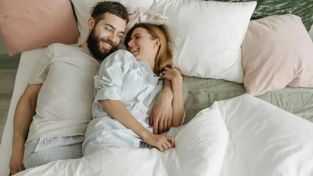 A couple lying in bed together, smiling and enjoying a cozy moment.