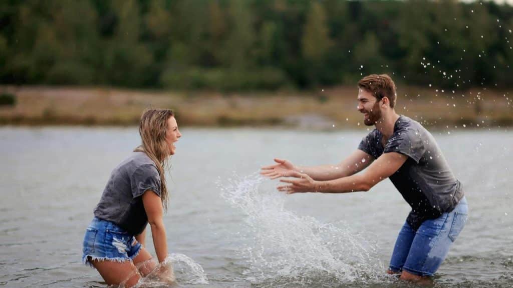 A couple laughing and splashing water at each other in a lake.