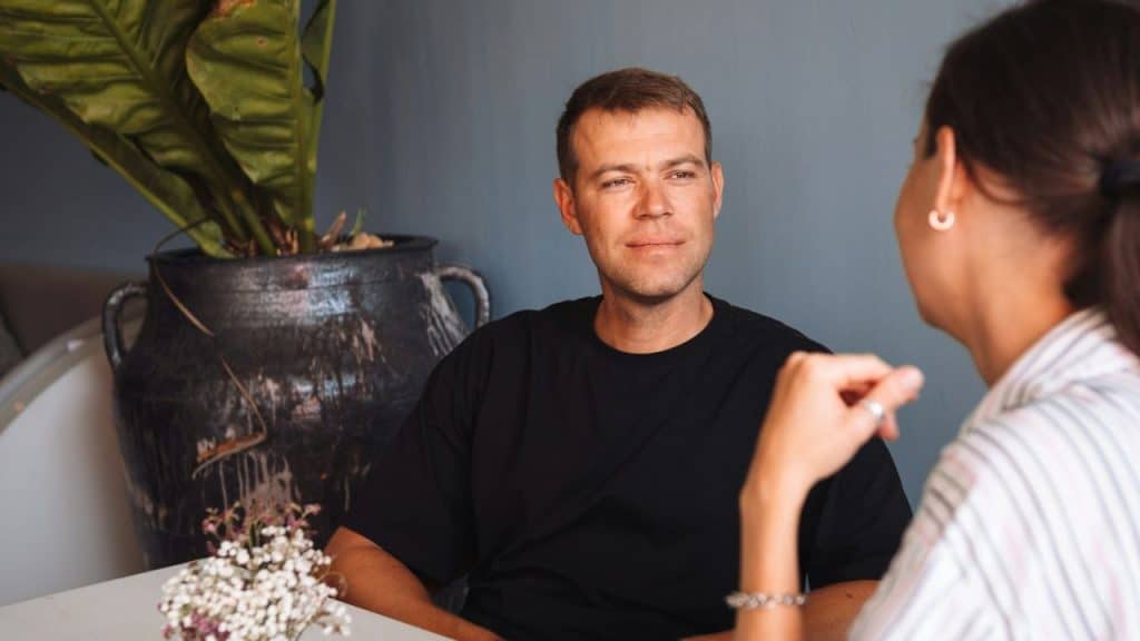 A man in a black shirt looks at a woman while sitting at a table.