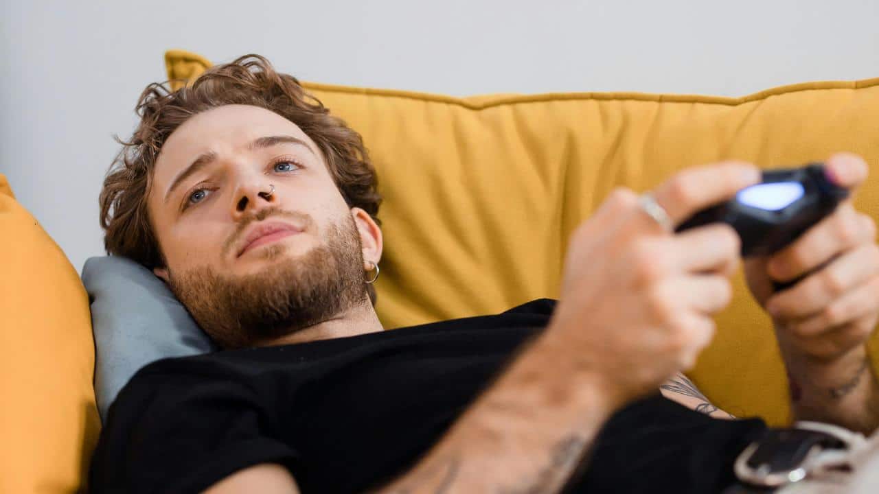A man lies on a couch holding a video game controller
