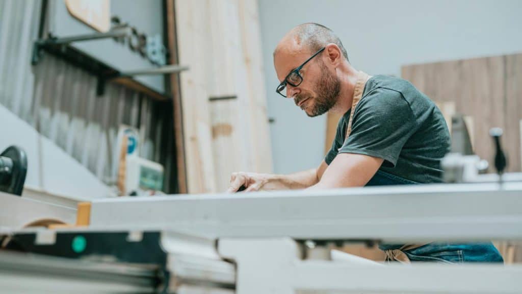 A man wearing glasses working with a tool at a woodworking bench.