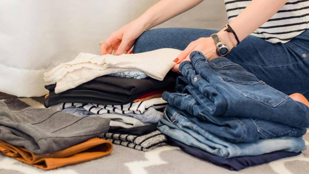 A person folding piles of clothes on the floor.