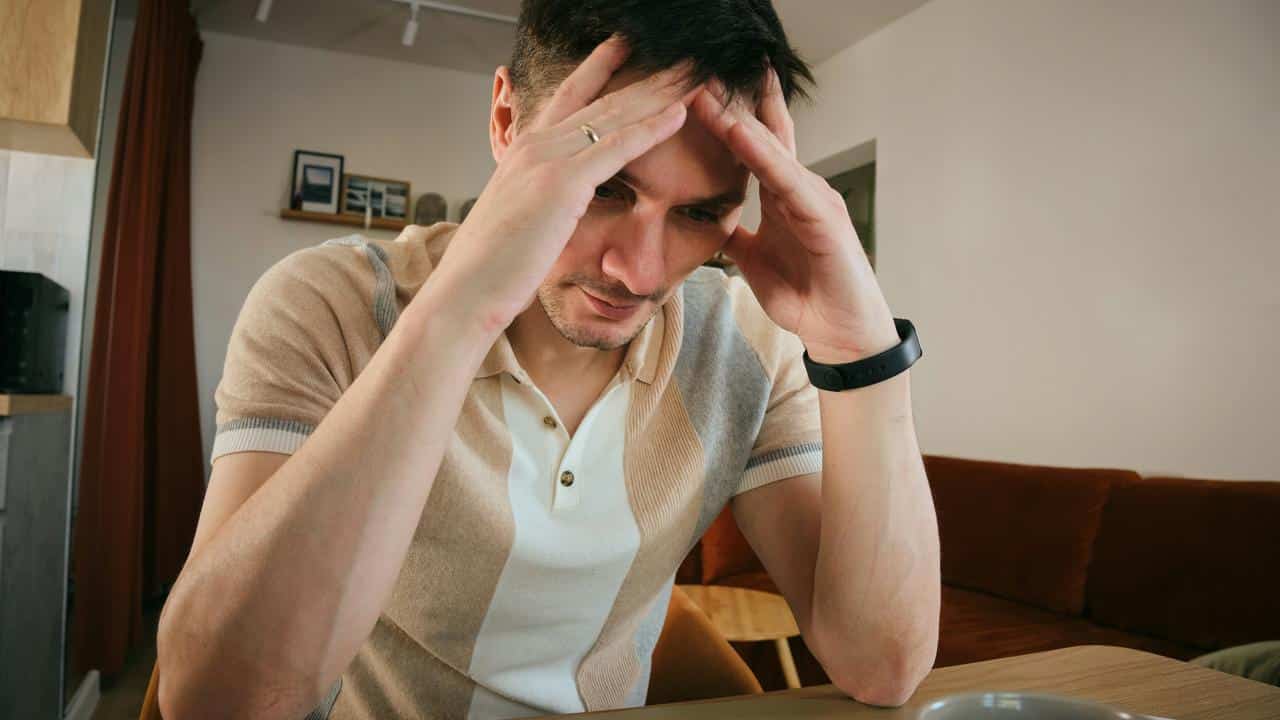 A man sits with his hands on his head looking stressed.