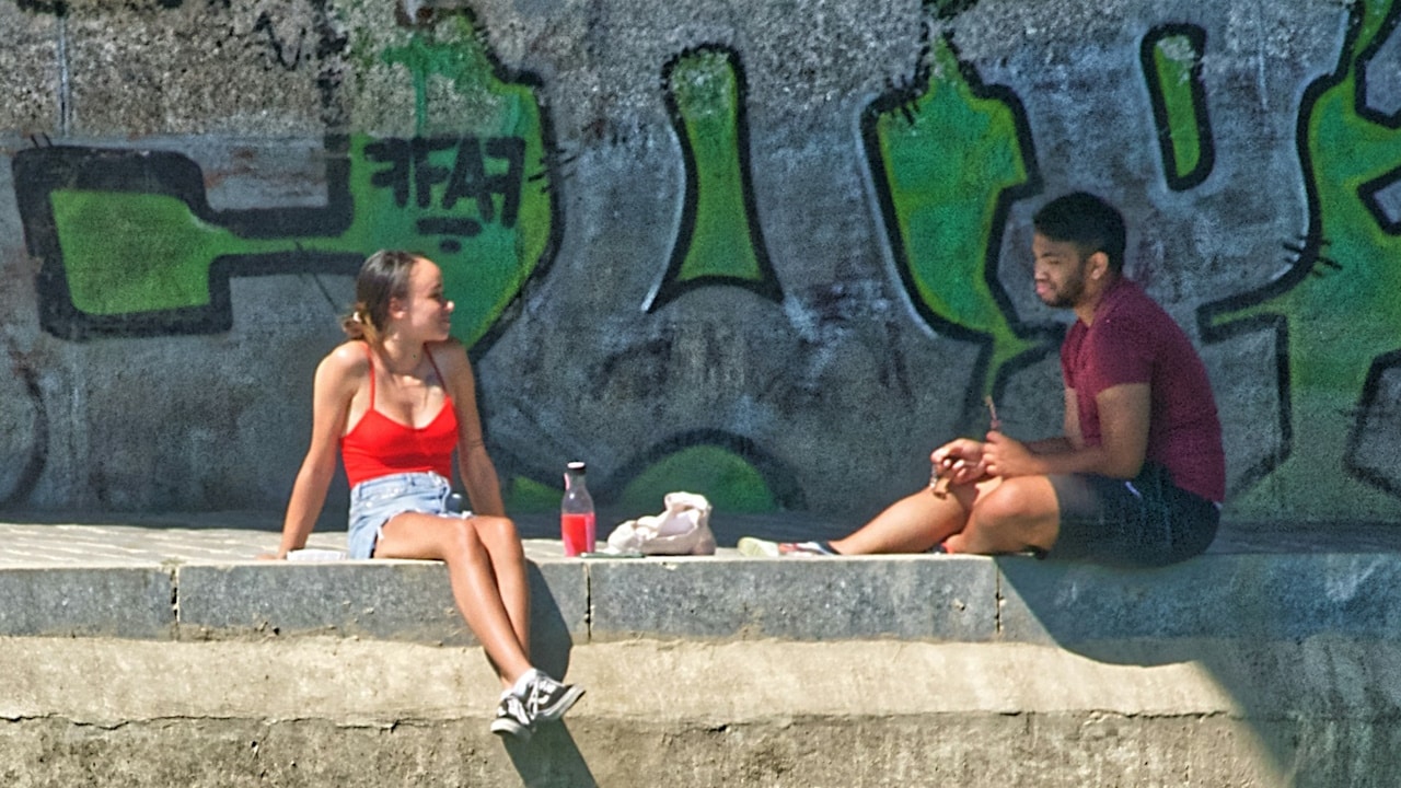 A woman in a red bikini sitting on a concrete bench beside a pool during the daytime.
