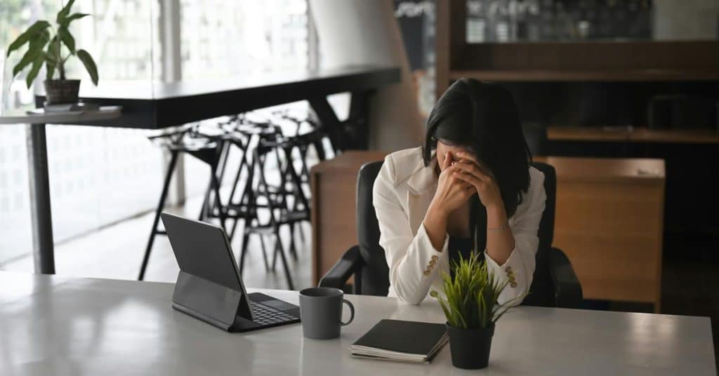 A stressed woman sitting at a desk with her head in her hands.