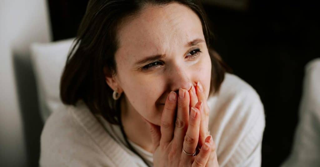 A woman holding her hands over her mouth with an emotional expression.