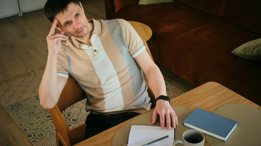 A man sitting at a table with a notebook, looking thoughtful.
