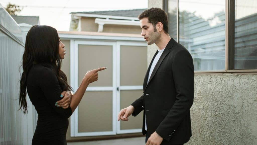 A woman in a black dress points her finger while talking to a man.