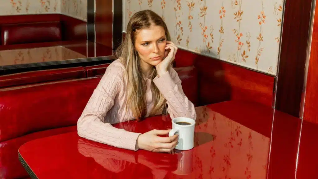 A woman sits alone at a red diner table, resting her head on her hand.