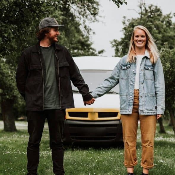 A couple holding hands while they are standing in a garden in front of a truck.