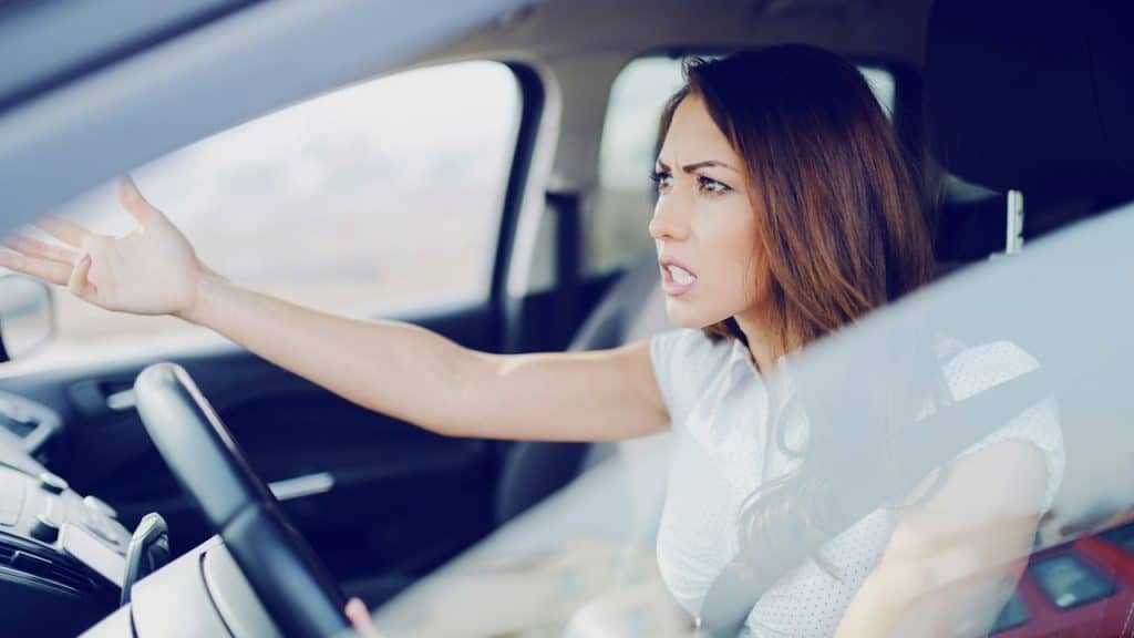 Angry attractive-caucasian-brunette yelling at other drivers while sitting in a car.