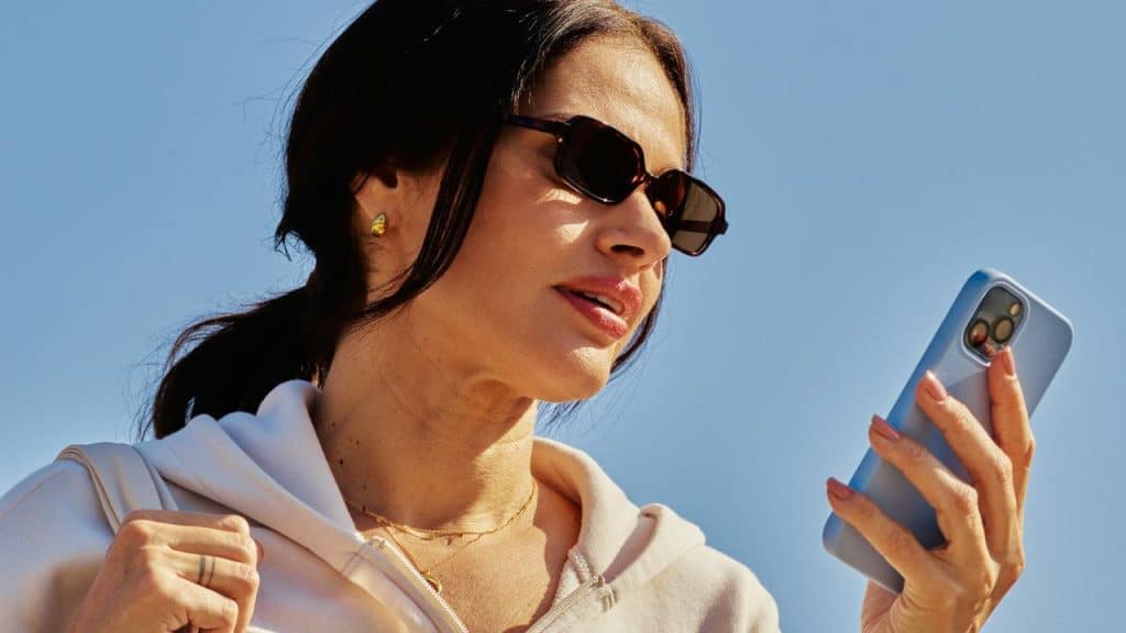 A woman wearing sunglasses and checking her smartphone outdoors.