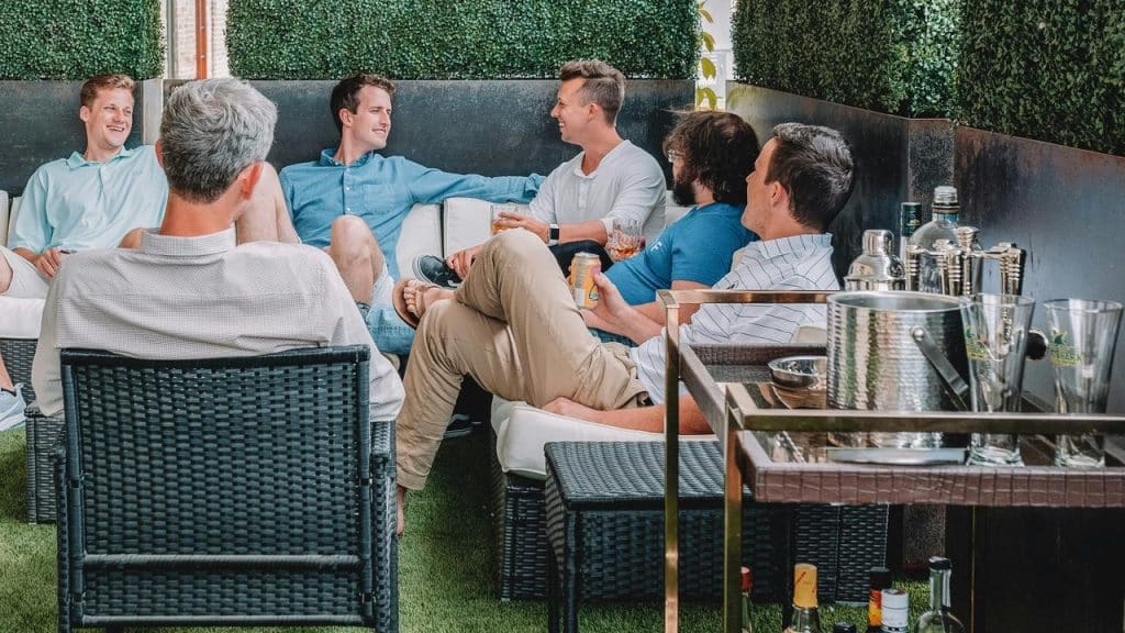 A group of men sitting together outdoors, chatting and drinking on a patio.