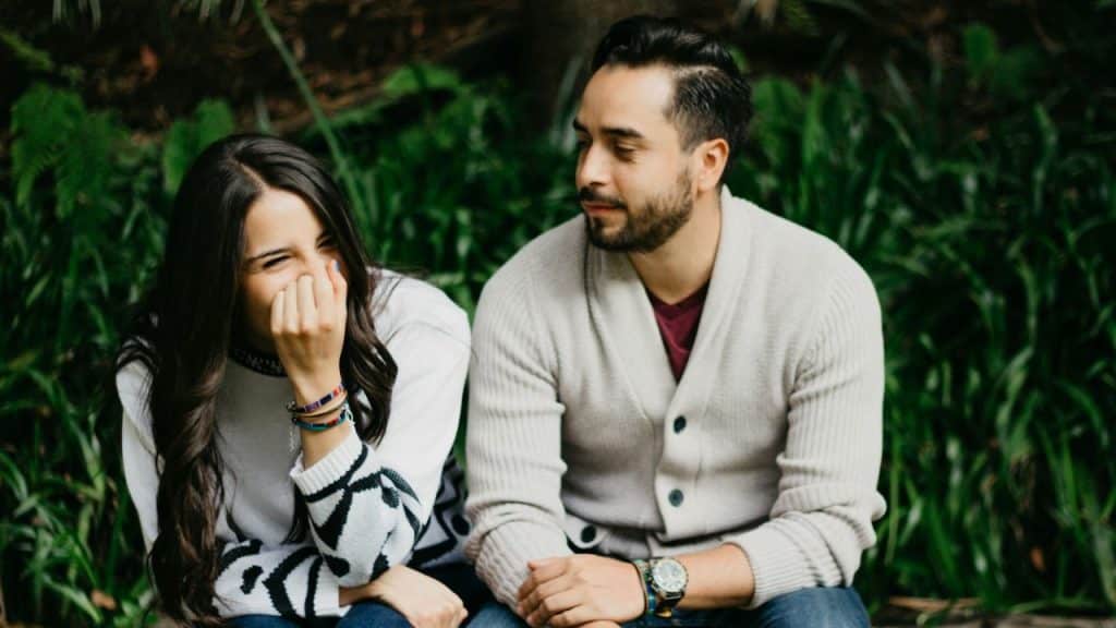 A man and woman sitting together outdoors with green foliage in the background.