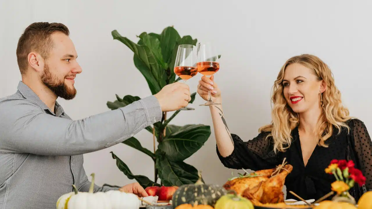 A man and woman toast with wine glasses over a table filled with autumn food.