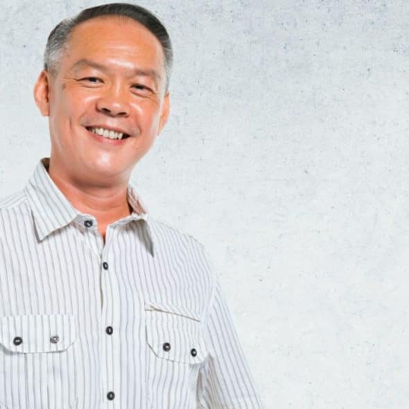 Smiling man with short salt-and-pepper hair wearing a striped button-down shirt against a textured wall.
