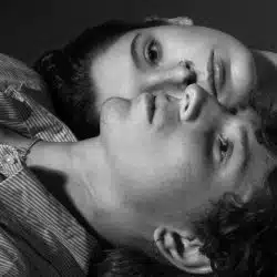 A couple lying vertically opposite to each other with their heads touching.