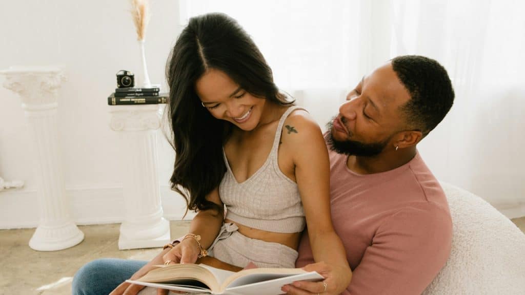 A man and woman sitting on a couch reading a book.