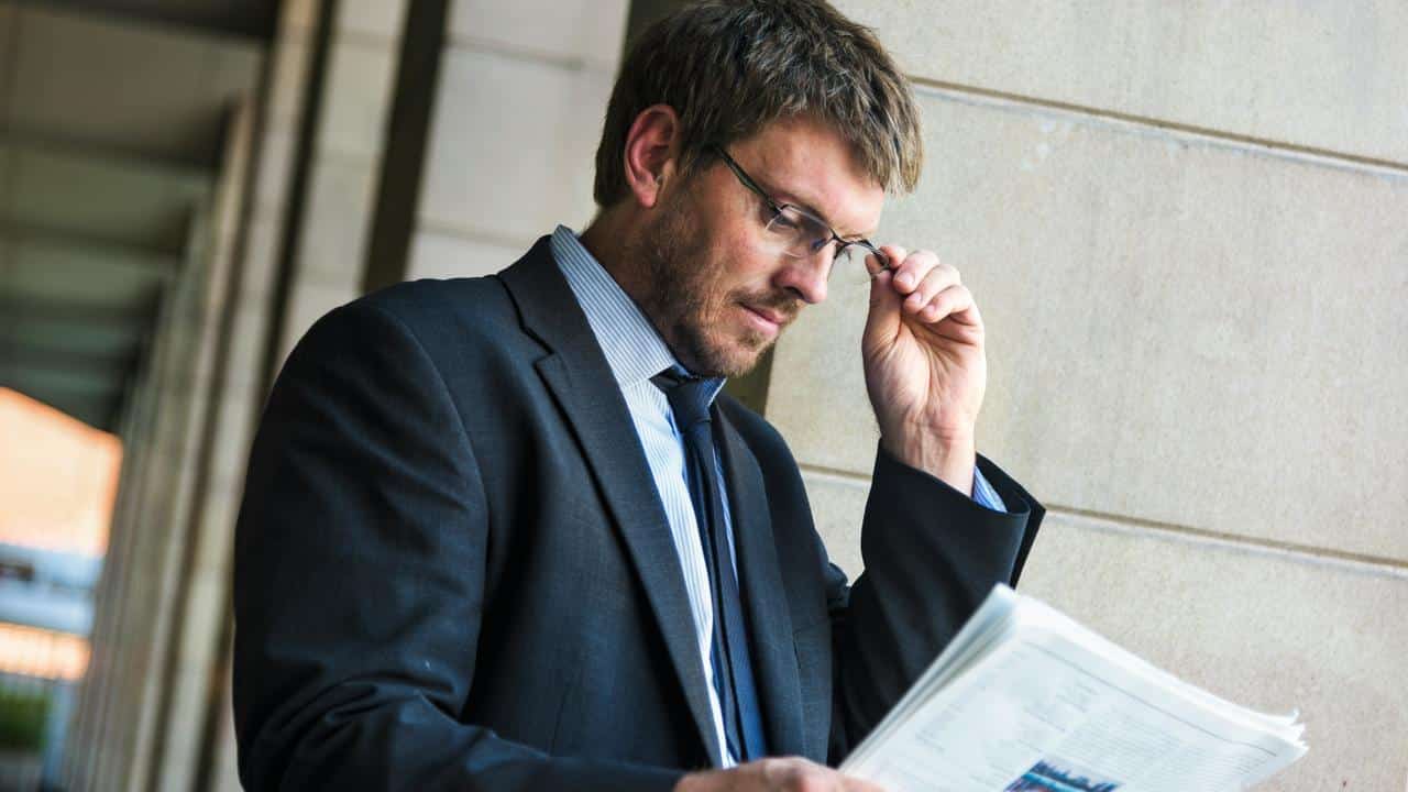 A man in a suit adjusting his glasses