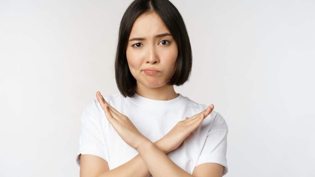 A woman with a displeased expression crossing her arms in an “X” gesture.