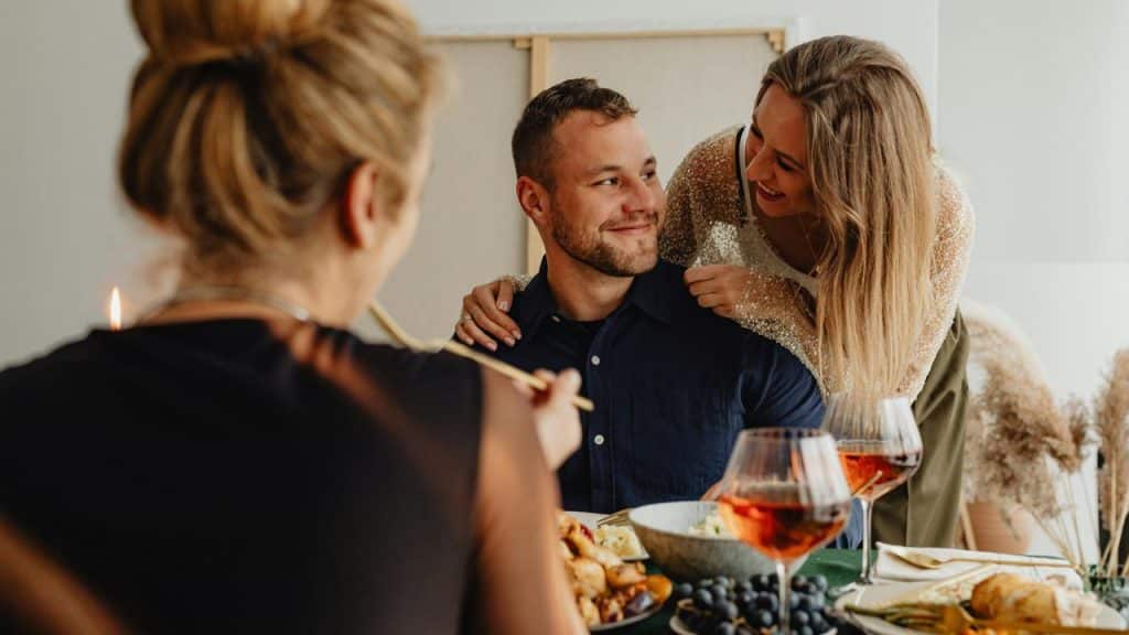 A woman leaning over a man’s shoulder as they smile during a meal with friends