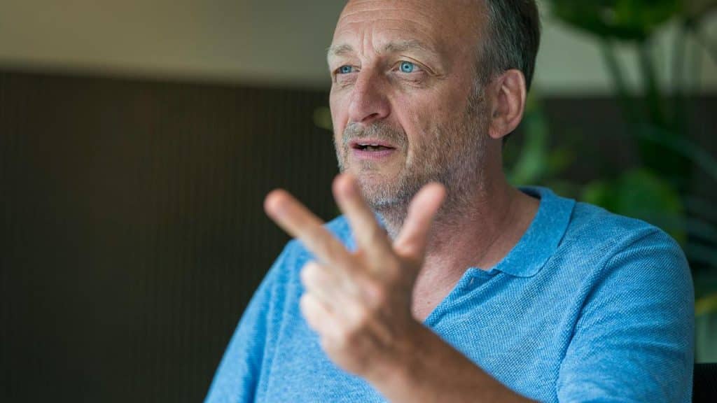 A middle-aged man gesturing while speaking indoors.