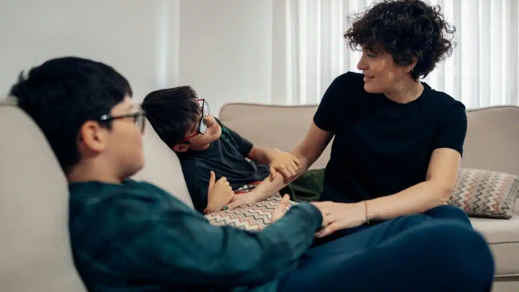 A woman sits on a couch talking and holding hands with two children.