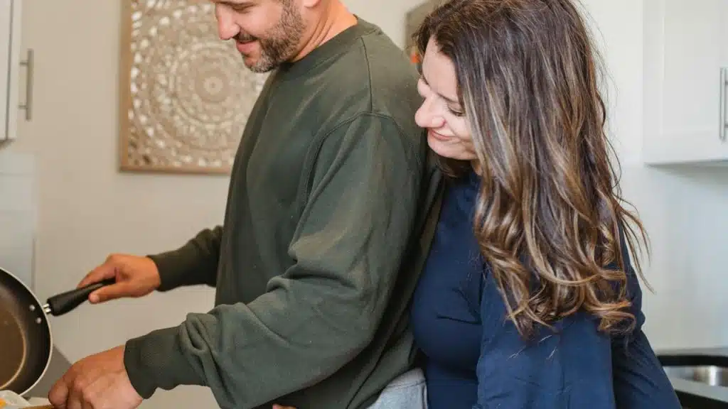 A couple cooking together in a kitchen, standing close and smiling.