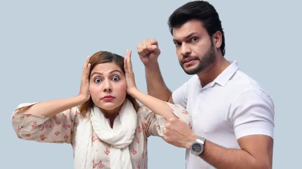 A bearded man brandishing his fists while a woman holds her hands on her ears and looks shocked.