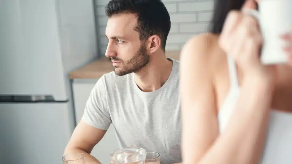 A man looks off-camera while a blurred person in the foreground holds a white mug.