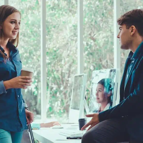 A woman holding a coffee talks with a man