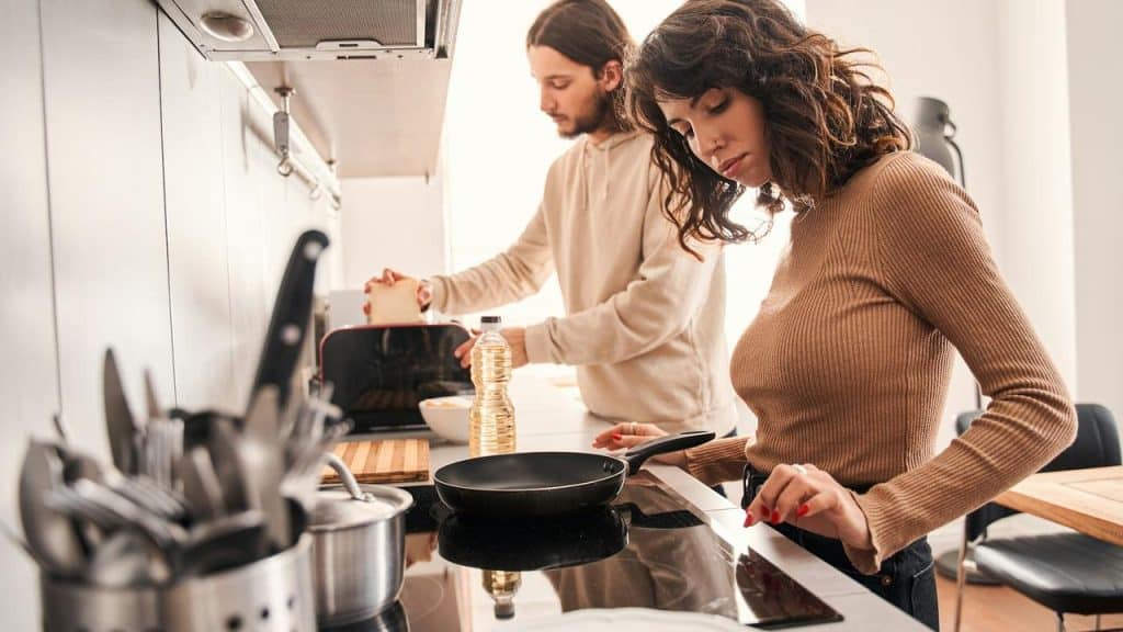 A woman cooking on a stove while a man prepares food behind her.