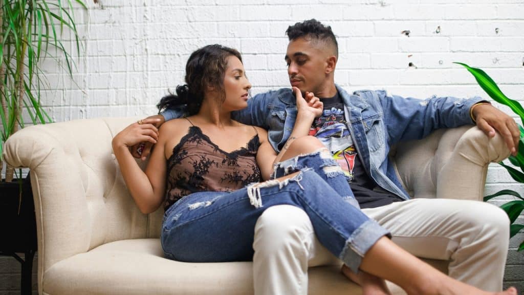 A couple sits on a couch together, facing each other while engaged in conversation.