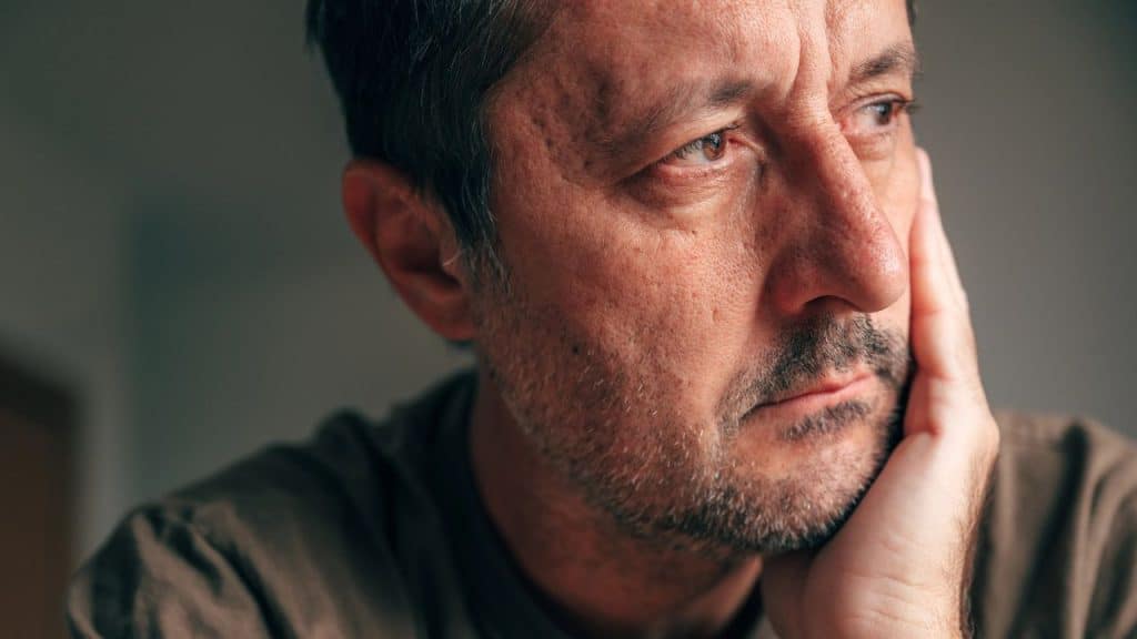 Close-up of a middle-aged man with stubble resting his chin on his hand.
