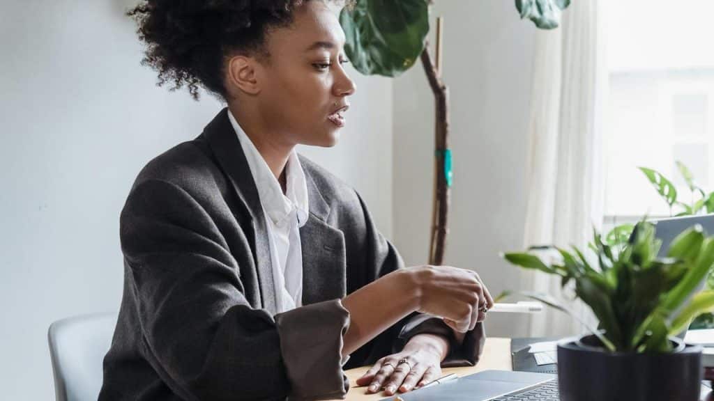 A woman working on a laptop at a desk with plants nearby.