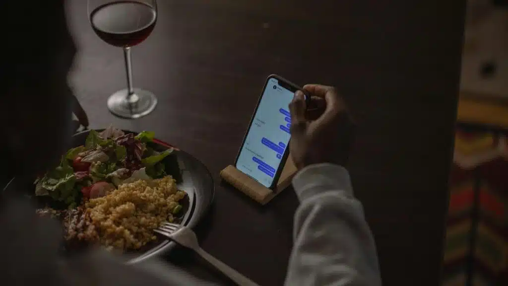 A person eating dinner while texting on a smartphone.