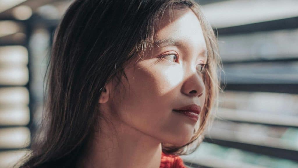 A woman gazing out a window with sunlight on her face.