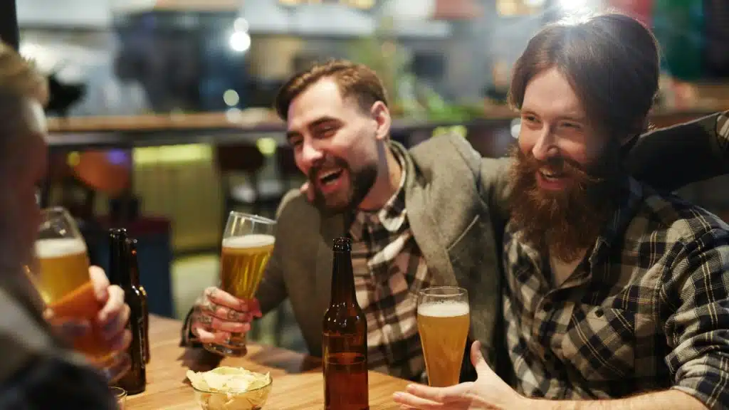 Three men drink beer and laugh together at a table in a pub.
