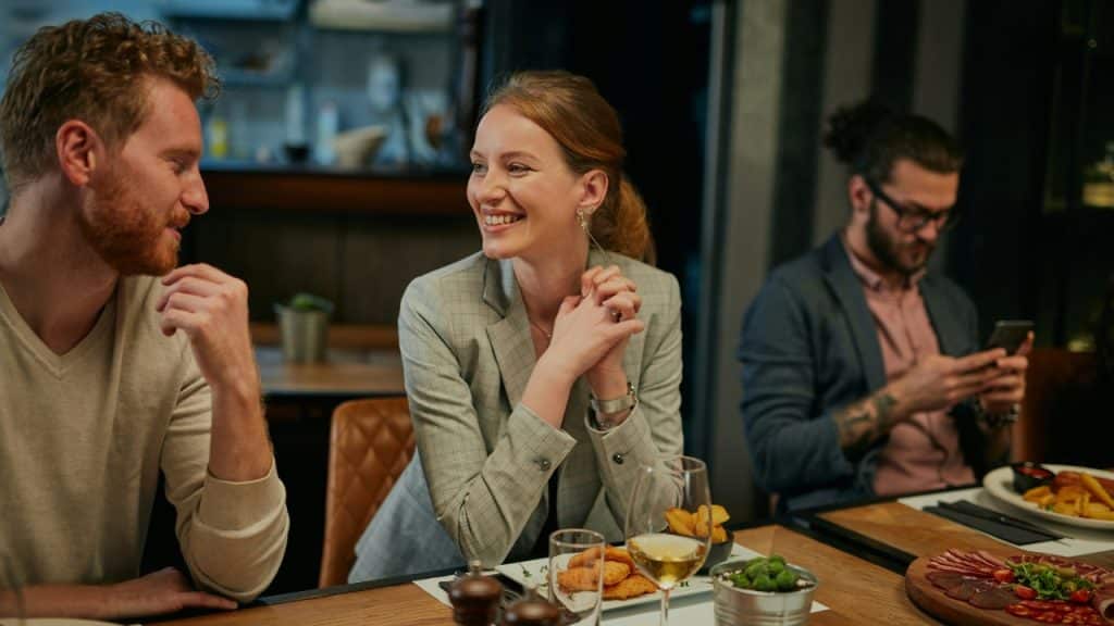 A woman in a grey blazer smiles at a man while sitting at a table.