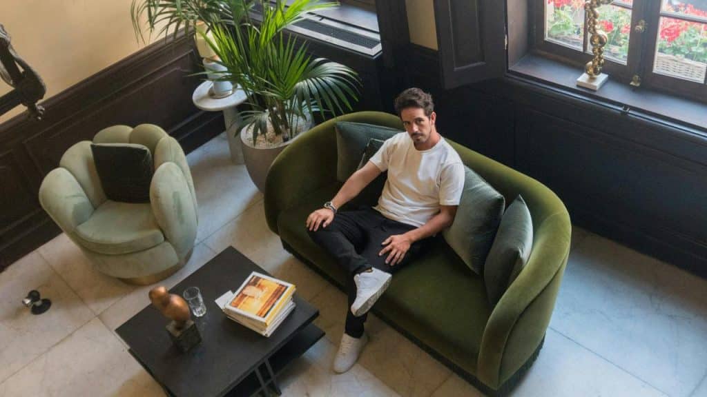 A man sitting on a green sofa in a stylish living room with plants and books.