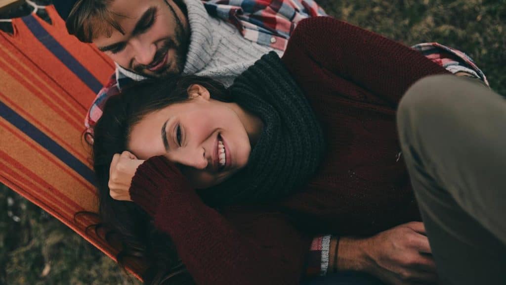 A happy couple lying together on a colorful striped blanket outdoors in the grass.