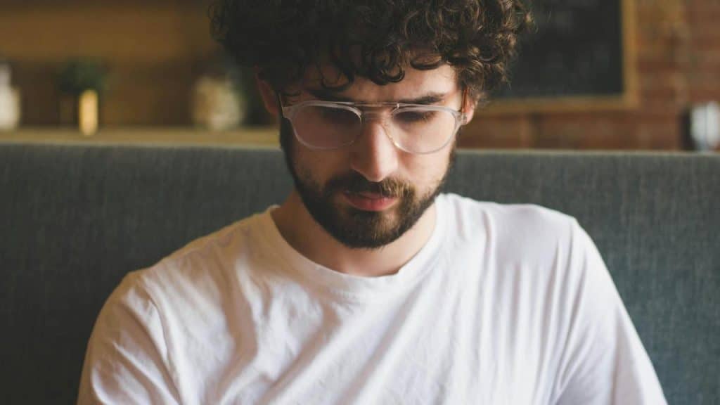 A man wearing glasses looking down at something while sitting indoors.