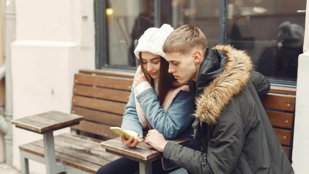 A couple sitting on a bench looking at a smartphone together.