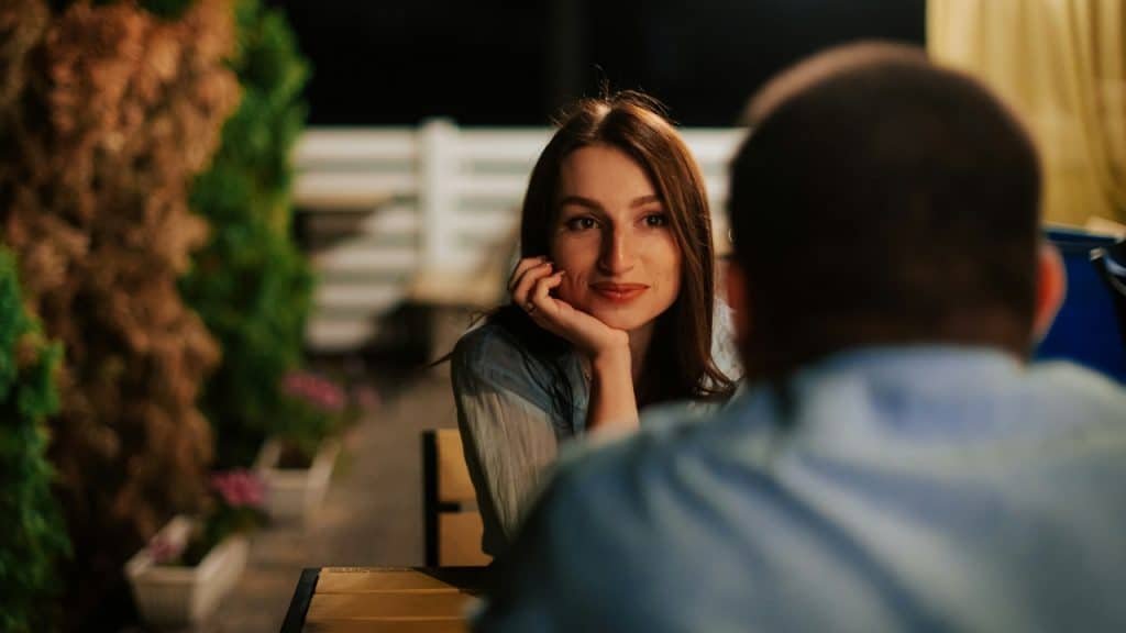 A woman rests her chin on her hand while looking at a blurred man.